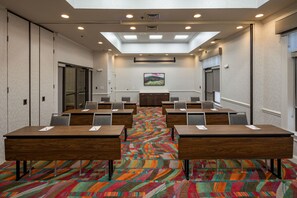 Un salón de conferencias con varias mesas y sillas, una alfombra colorida y un techo con tragaluces.