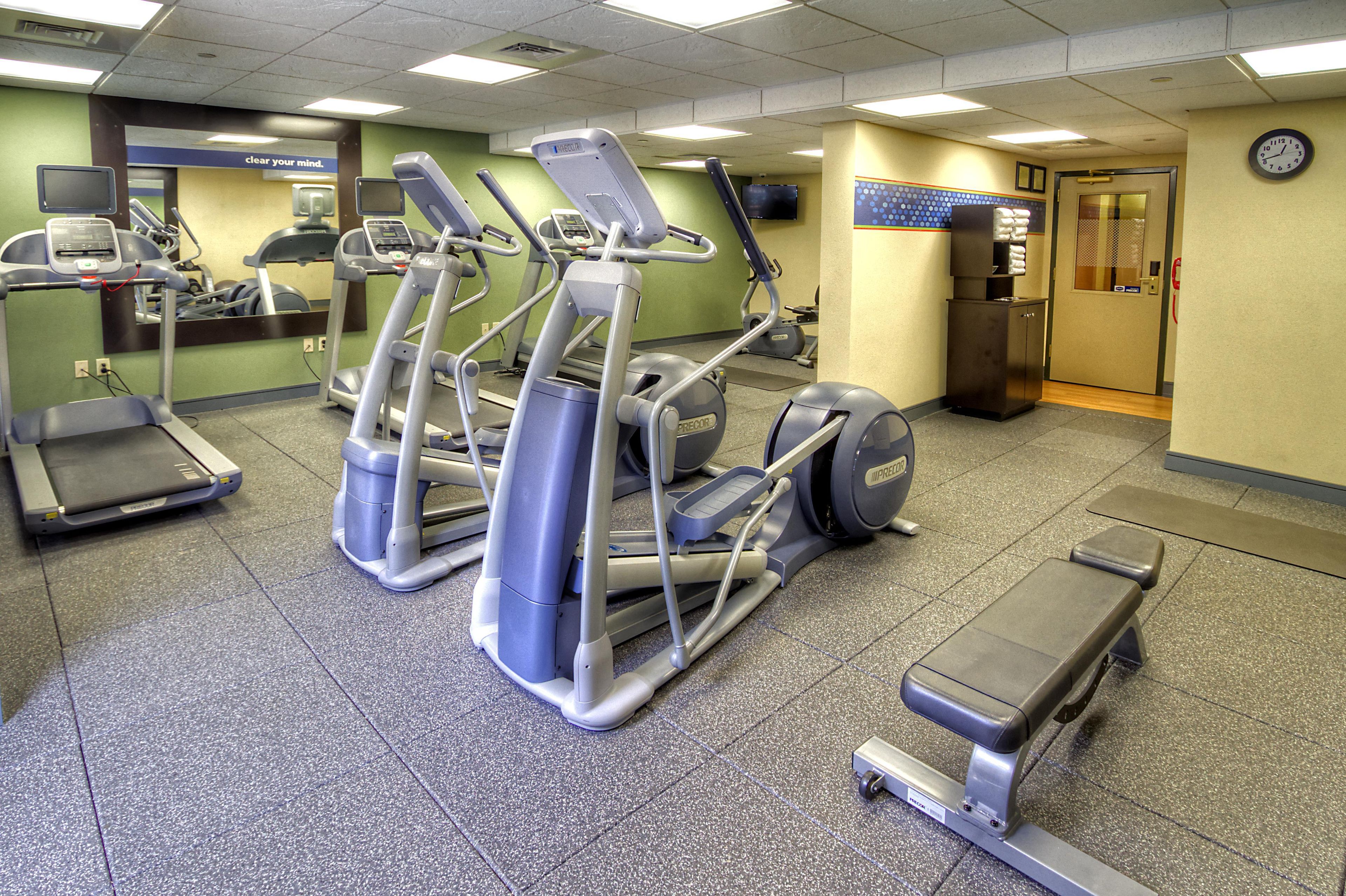 Un gimnasio con cintas de correr, elípticas y una banca para pesas.