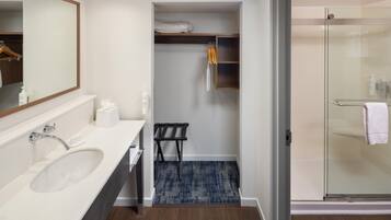 A modern bathroom with a large sink, a mirror, a shower, and a small seating area.