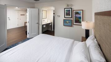 Una habitación de hotel con una cama grande, una mesita de noche con lámpara, un reloj de pared y cuadros enmarcados.