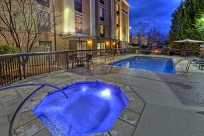 Un espace piscine d’hôtel comprenant un jacuzzi, des chaises longues et un foyer extérieur.