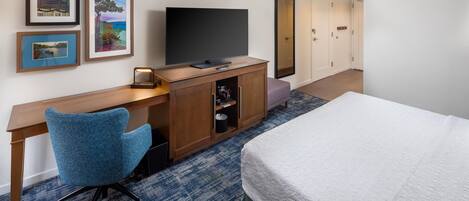 Una habitación de hotel con una cama, un escritorio con televisor, una silla y cuadros en la pared.