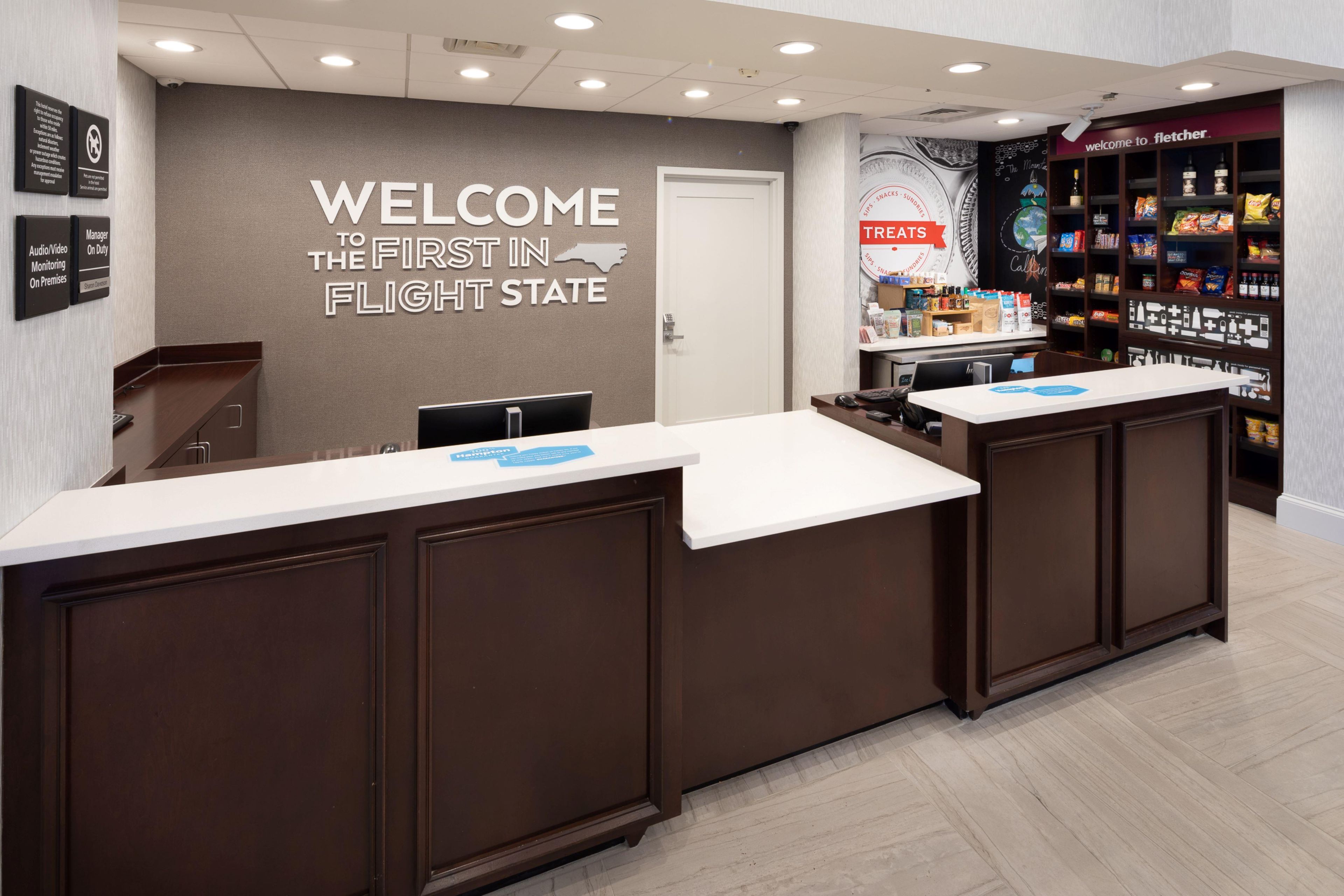 A reception desk with a 'Welcome to the First in Flight State' sign, a snack bar, and a security desk.