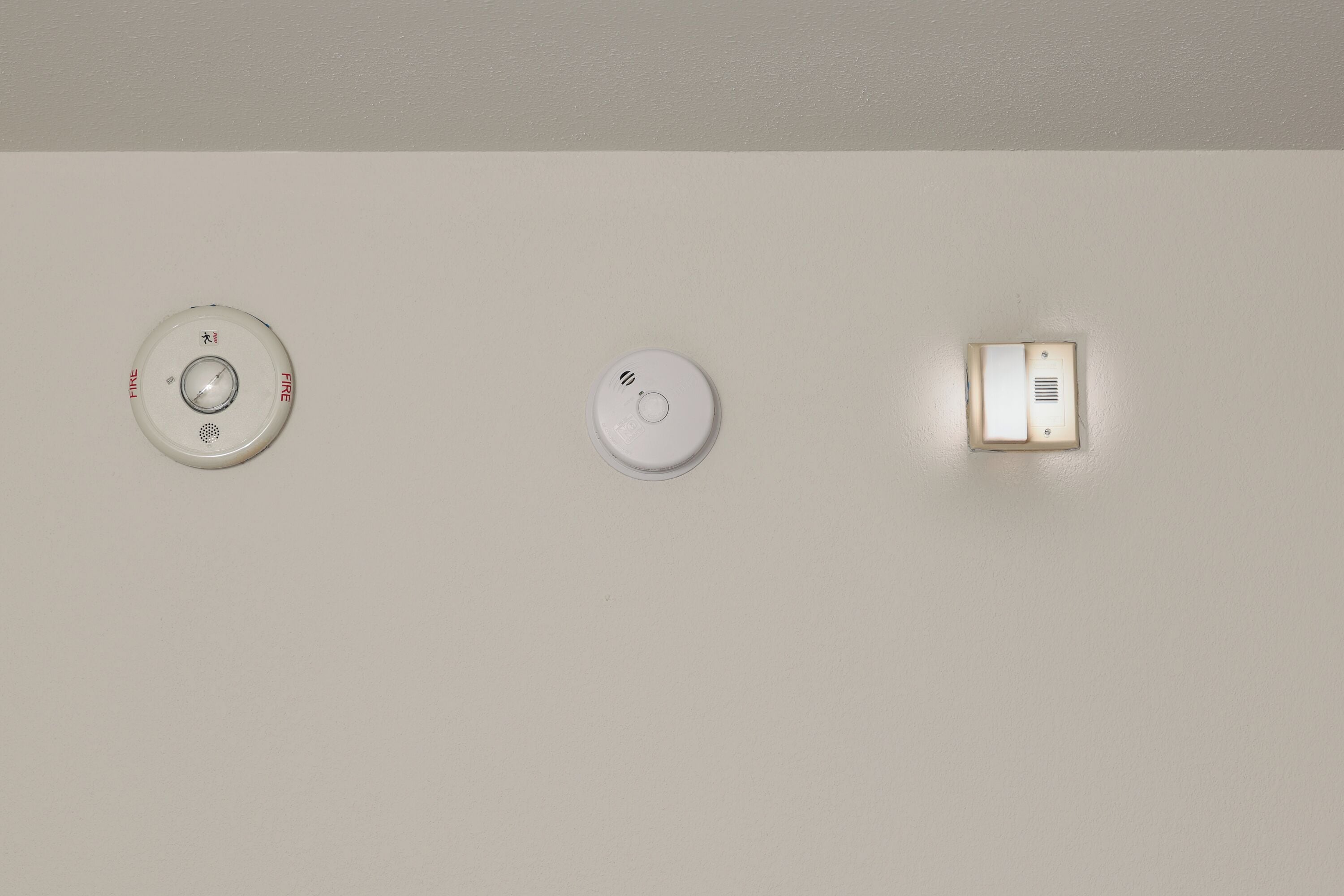 Três dispositivos fixados na parede: um detector de fumaça, um detector de monóxido de carbono e um painel de segurança.