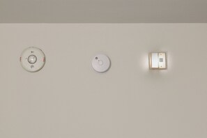 Drei an der Wand montierte Geräte: ein Rauchmelder, ein Kohlenmonoxidmelder und eine Sicherheitstafel.