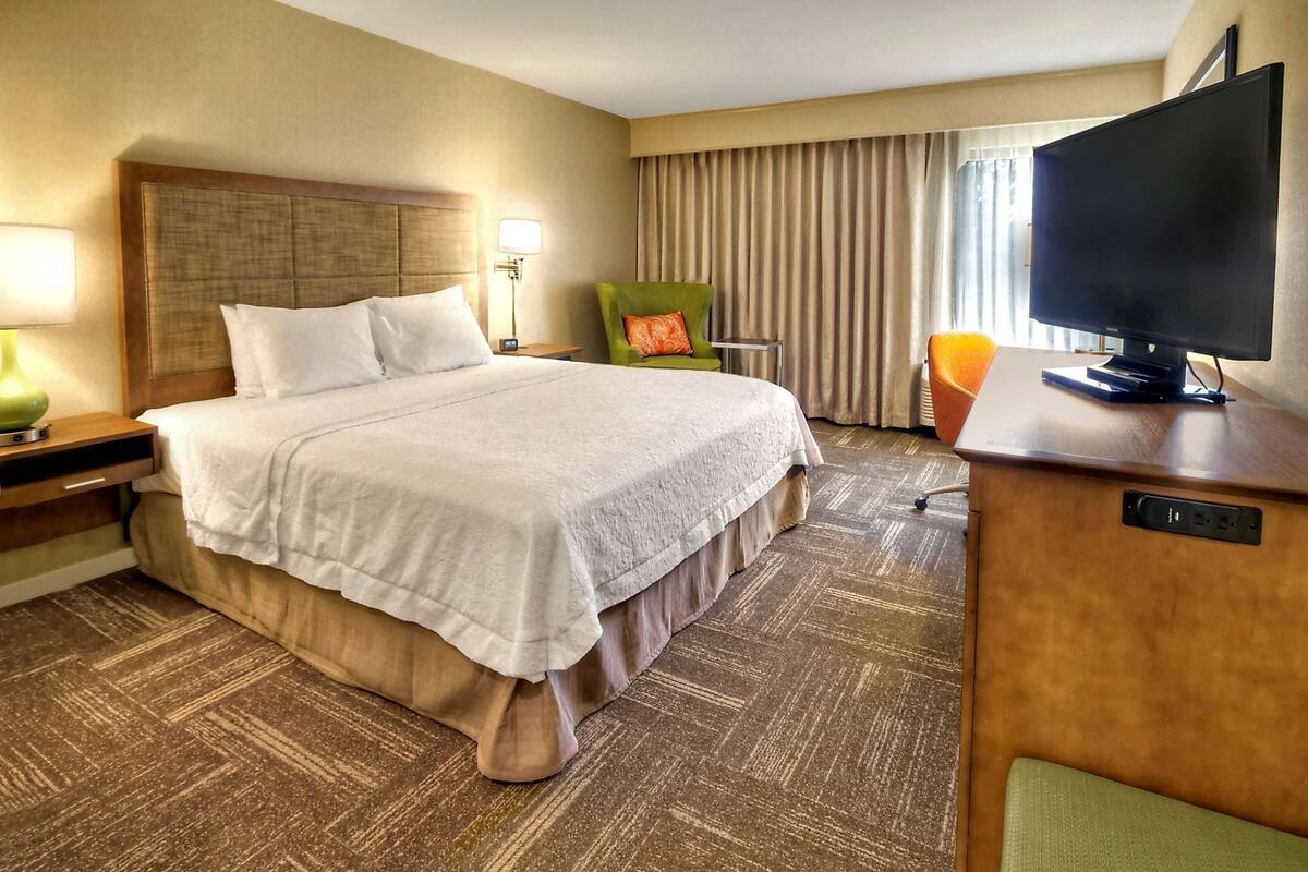 Habitación de hotel con una cama grande, televisión, escritorio con computadora, silla y lámpara.