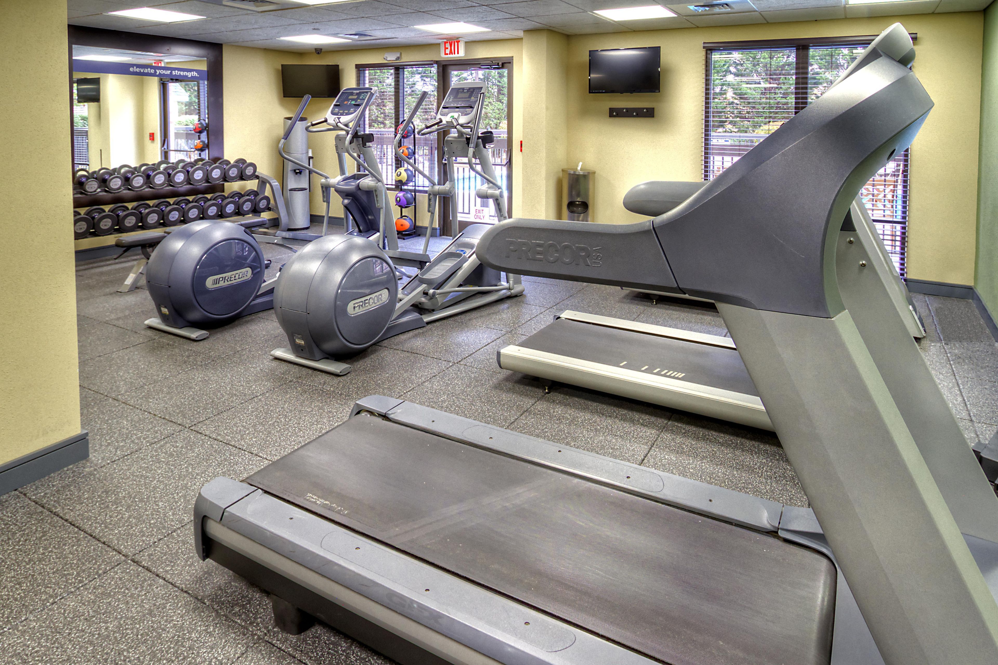 A gym with treadmills, elliptical machines, and a wall-mounted TV.