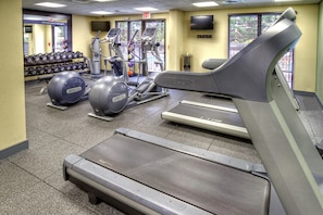 Ein Fitnessraum mit Laufbändern, Crosstrainern und einem an der Wand befestigten Fernseher.