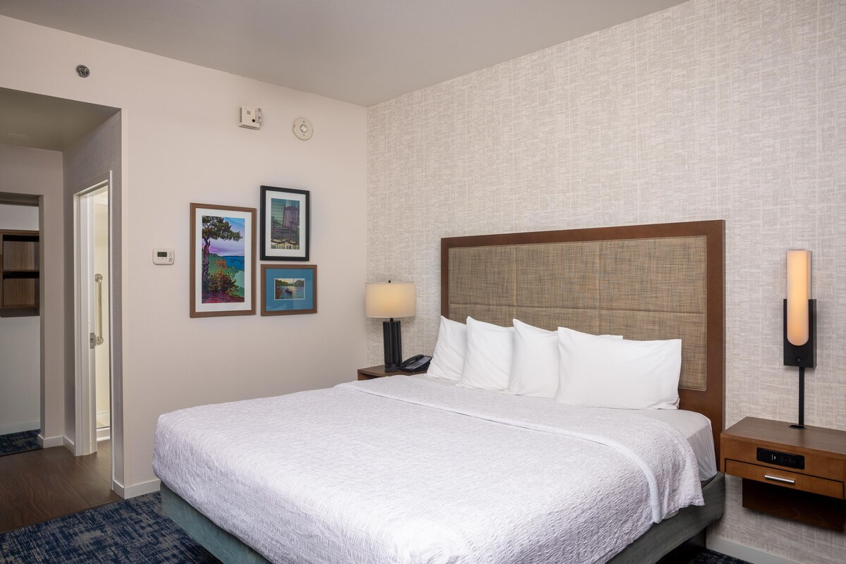 Ein Hotelzimmer mit einem großen Bett, einem Nachttisch mit Lampe und drei gerahmten Bildern an der Wand.