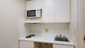 A compact kitchenette with a microwave, sink, and cabinets. - Suburban Studios Winston Salem-University Parkway (Winston-Salem)