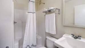 A bathroom with a toilet, sink, and shower curtain. - Suburban Studios Winston Salem-University Parkway (Winston-Salem)