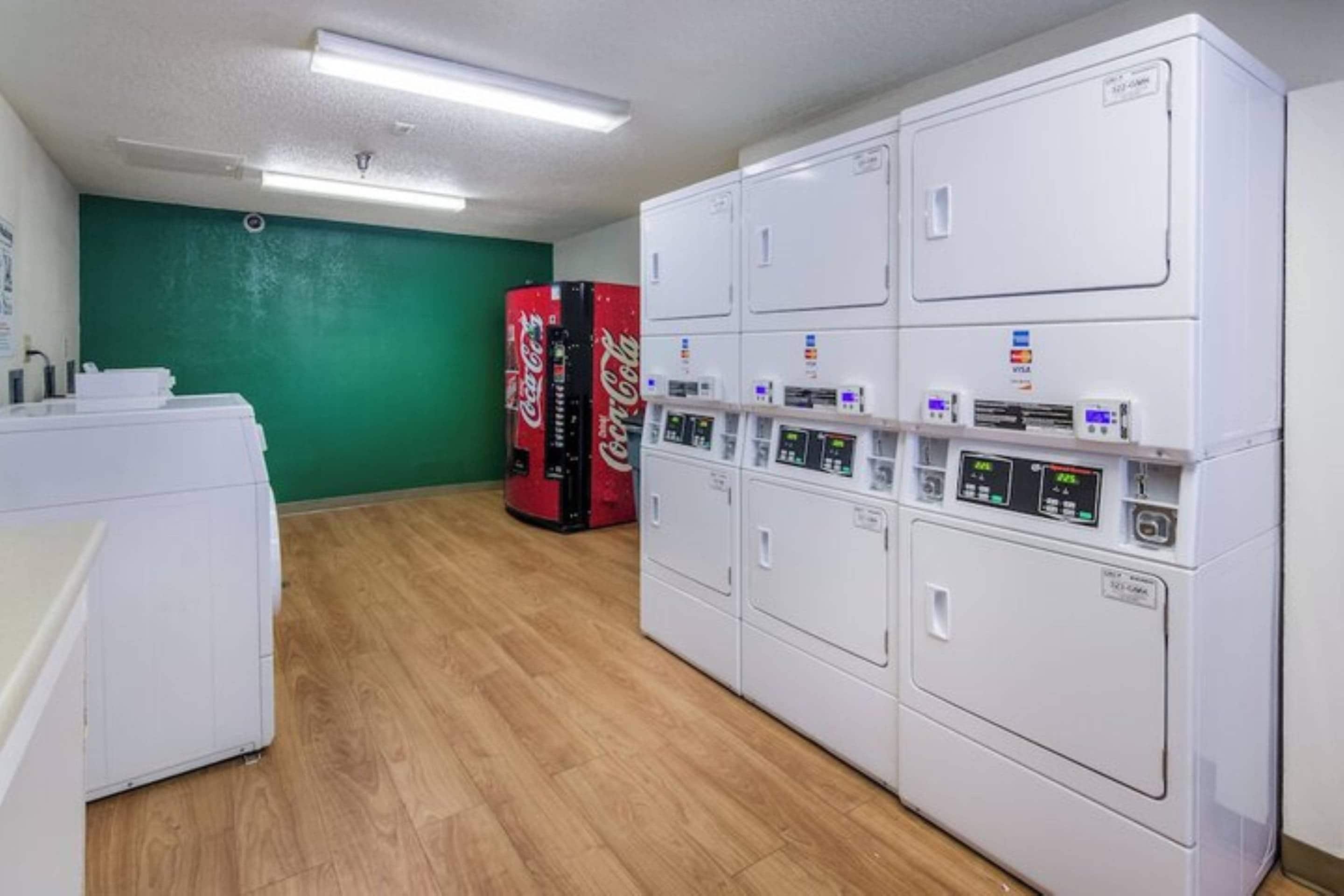 Un área de lavandería con varias lavadoras y secadoras, una pared verde y suelo de madera.