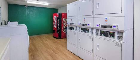 A laundry area with multiple washing machines and dryers, a green wall, and a wooden floor.