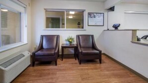 A room with two leather chairs, a small table with a vase, a window, and a wall-mounted display. - Suburban Studios Winston Salem-University Parkway (Winston-Salem)
