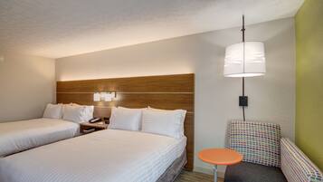 A hotel room with two beds, a nightstand, a small table, and a colorful chair.