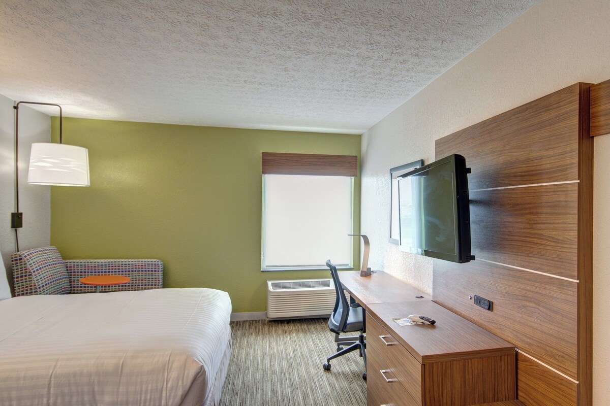 A hotel room with a bed, a desk, a chair, a television, and a window.