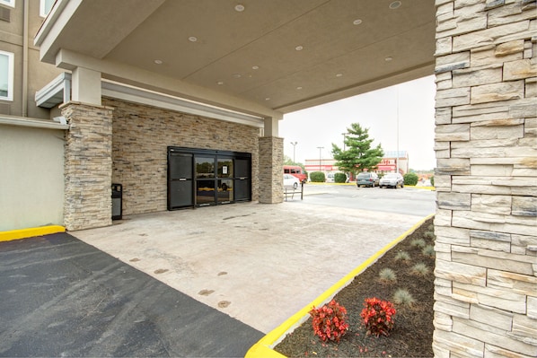 Un bâtiment doté d’une façade en pierre, d’une entrée abritée et d’un parking délimité par une ligne jaune.