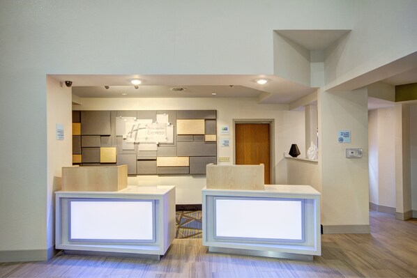 A reception area with a modern design, featuring a reception desk, a wall-mounted information board, and a wooden door. - Holiday Inn Express Columbus South - Obetz by IHG (Columbus)