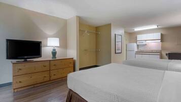 A hotel room with a bed, a TV, a dresser, a bathroom, and a kitchenette.