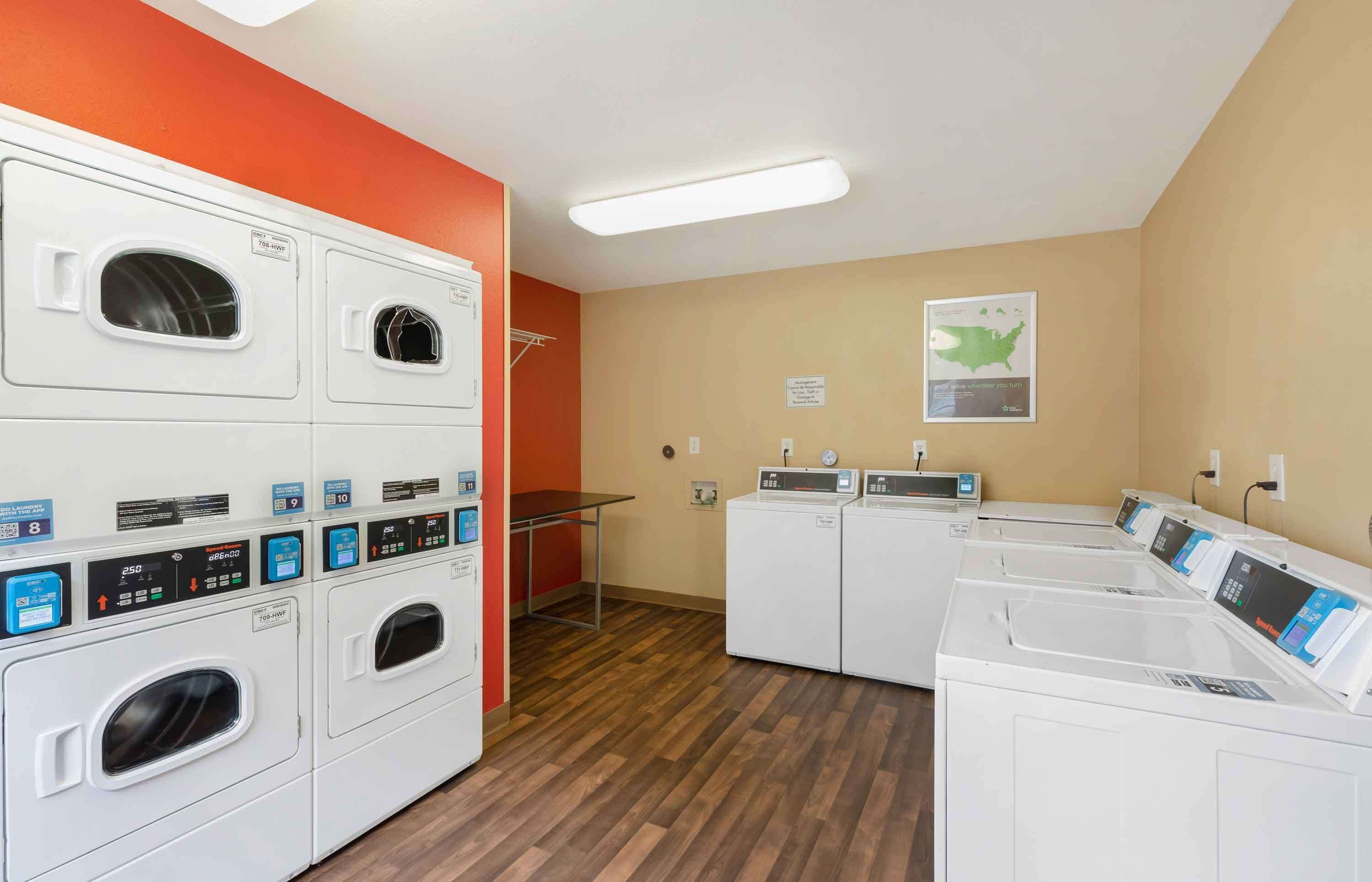 A laundry facility with multiple washing machines and dryers, a table, and a map on the wall.