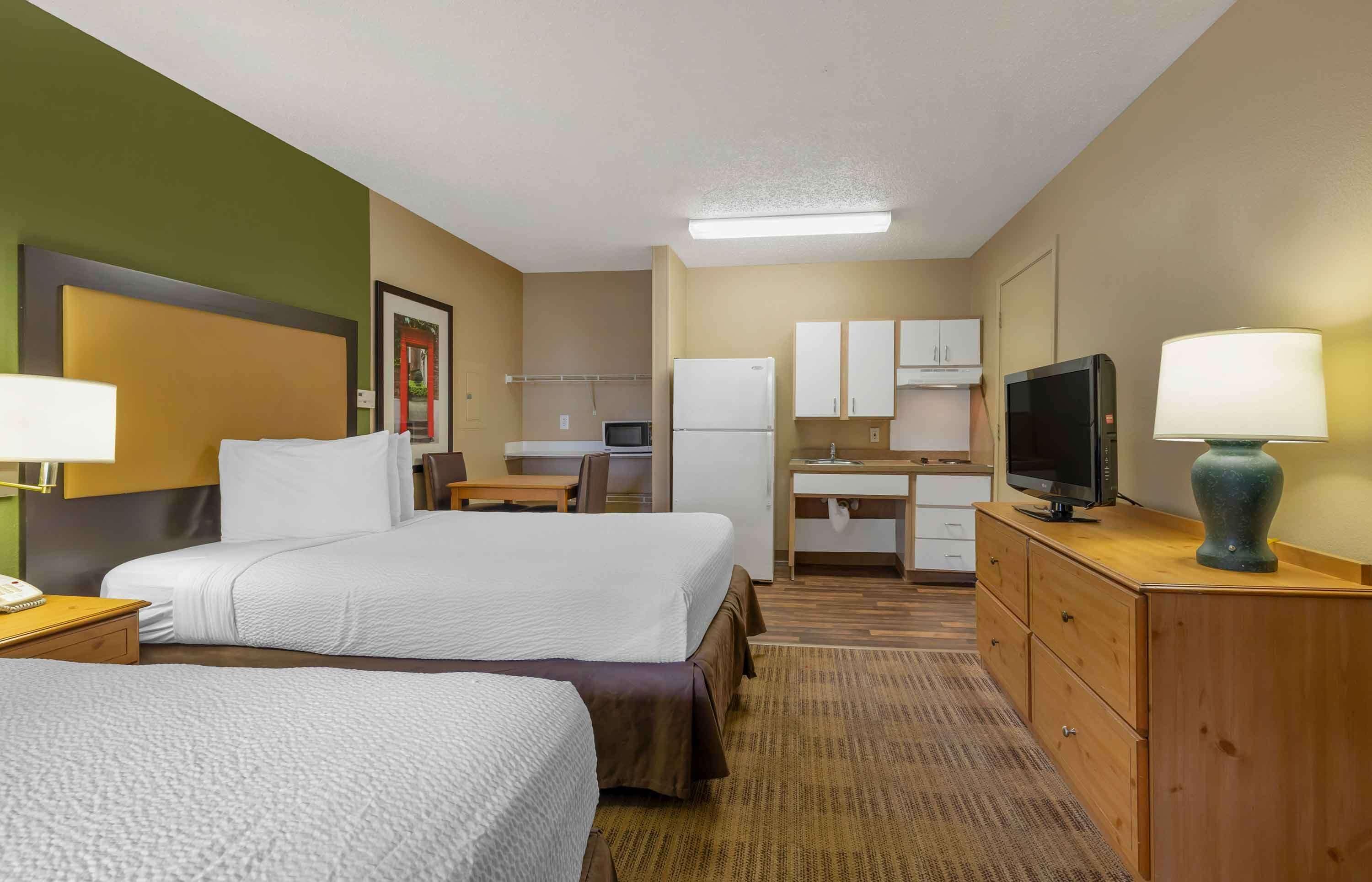 Habitación de hotel con dos camas, un escritorio, televisión y kitchenette.