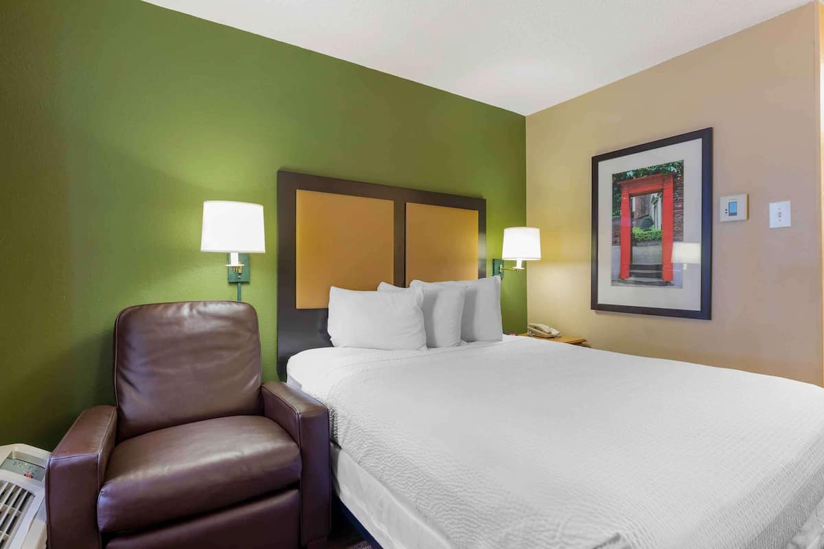 Une chambre d’hôtel avec un grand lit, deux lampes de chevet, un fauteuil en cuir marron et un tableau encadré au mur.