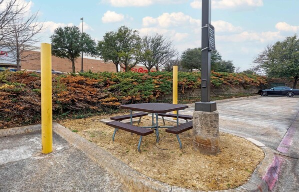 A picnic table with benches, surrounded by a landscaped area with bushes and trees.