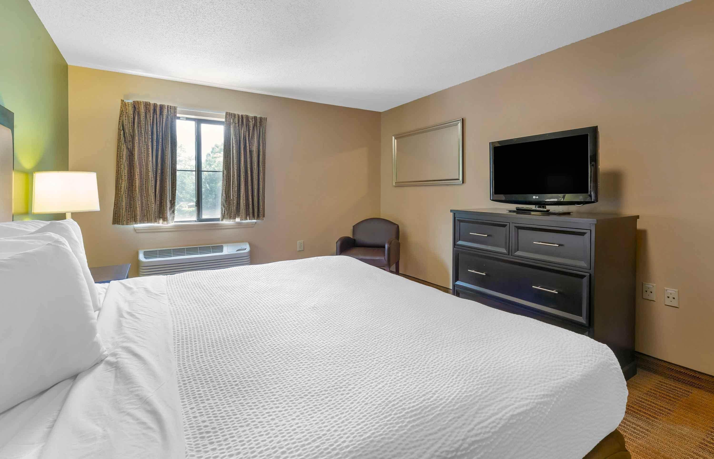Habitación de hotel con una cama grande, un escritorio con lámpara, una silla, un televisor y un aparador.