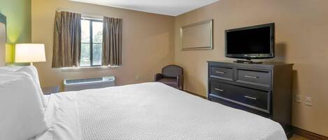 Habitación de hotel con una cama grande, un escritorio con lámpara, una silla, un televisor y un aparador.