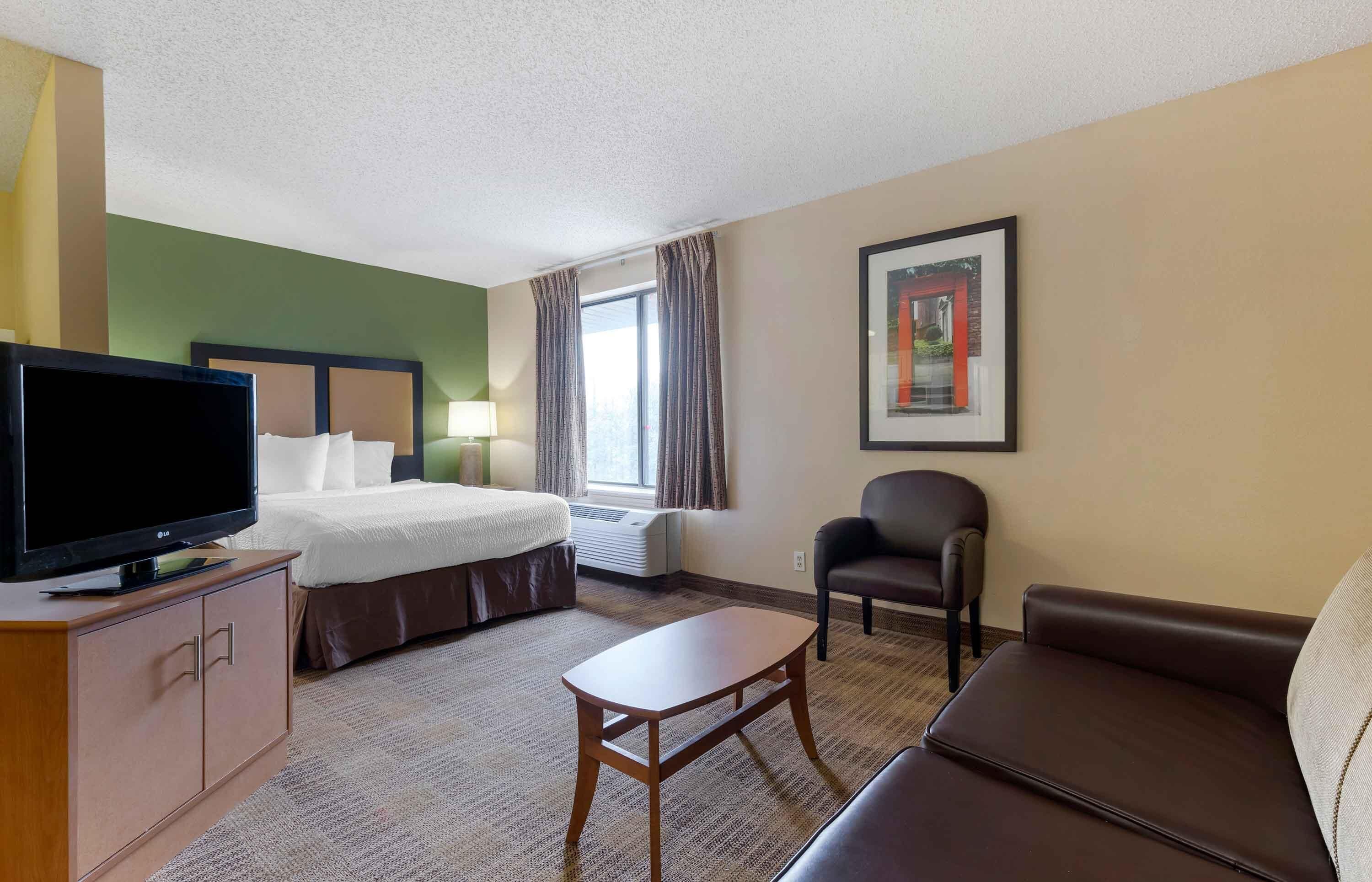 A hotel room with a bed, a television, a desk, a chair, and a sofa.
