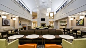 A spacious lobby with a central seating area, multiple tables, and a high ceiling with hanging lights. - Homewood Suites by Hilton Dulles Int'l Airport (Herndon)