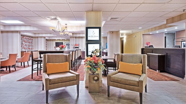 A hotel lobby with two armchairs, a reception desk, a dining area, and a large screen. - Hampton Inn Huntington/Barboursville (Barboursville)