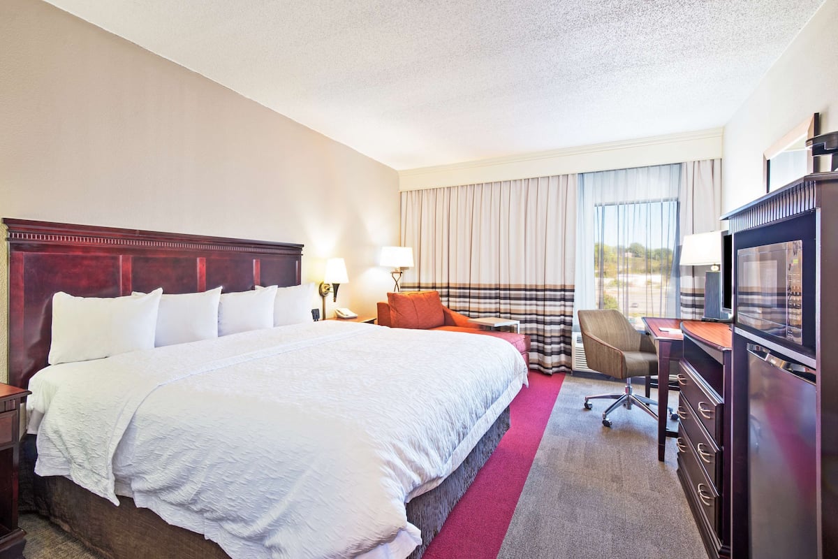 A hotel room with a large bed, a desk with a television, a chair, and a window with curtains.