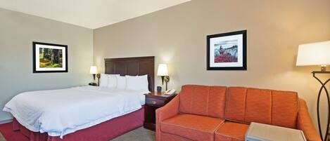 A hotel room with a bed, a sofa, two bedside tables with lamps, and two framed pictures on the walls.