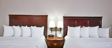 A hotel room with two beds, a nightstand with a lamp, and a phone.