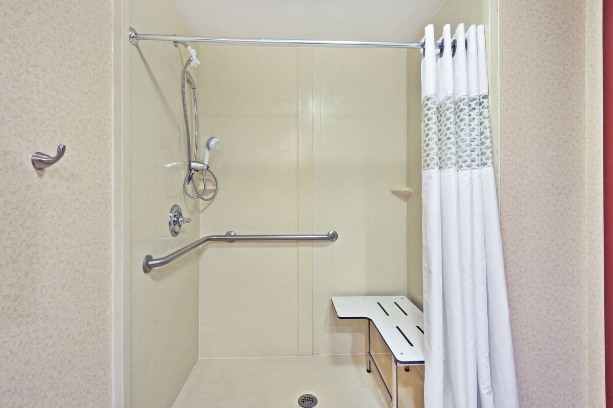 A shower area with a grab bar, a showerhead, and a white curtain.