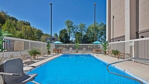 A swimming pool with lounge chairs and umbrellas, surrounded by a fence and trees. - Hampton Inn Huntington/Barboursville (Barboursville)