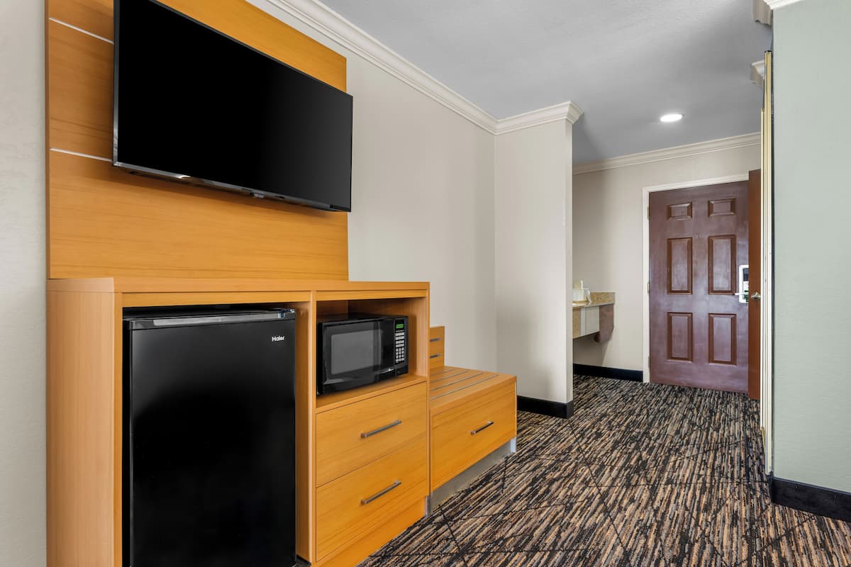 A hotel room with a flat-screen TV, a refrigerator, a microwave, and a wooden dresser.