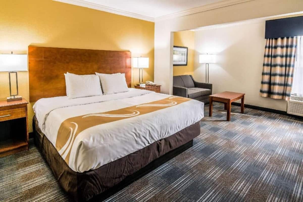 A hotel room with a large bed, two bedside tables, a desk, a chair, and a window with curtains.