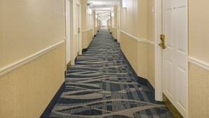 Ein Hotelgang mit Teppichböden, Türen auf beiden Seiten und Leuchten an der Decke.