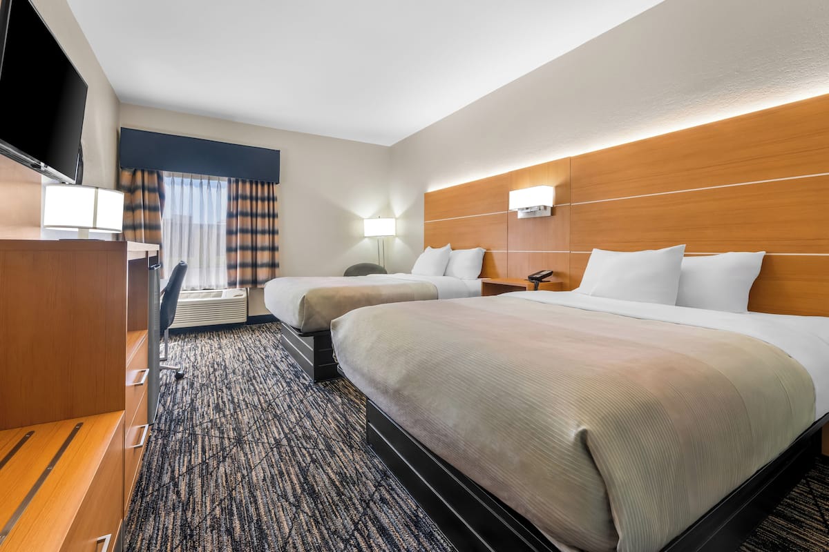 A hotel room with two beds, a desk, a TV, and a lamp.