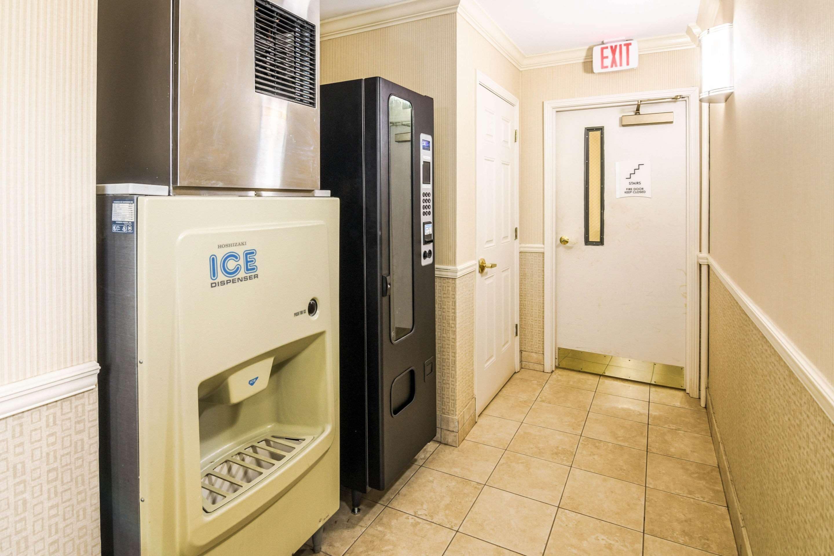 A hallway with an ice dispenser, a refrigerator, and an exit door with a sign.