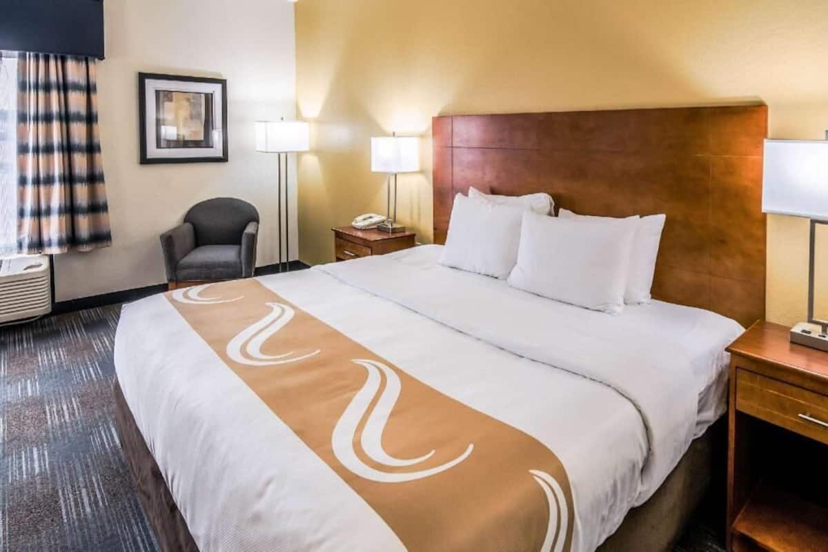 A hotel room with a large bed, a chair, bedside lamps, and a framed picture on the wall.