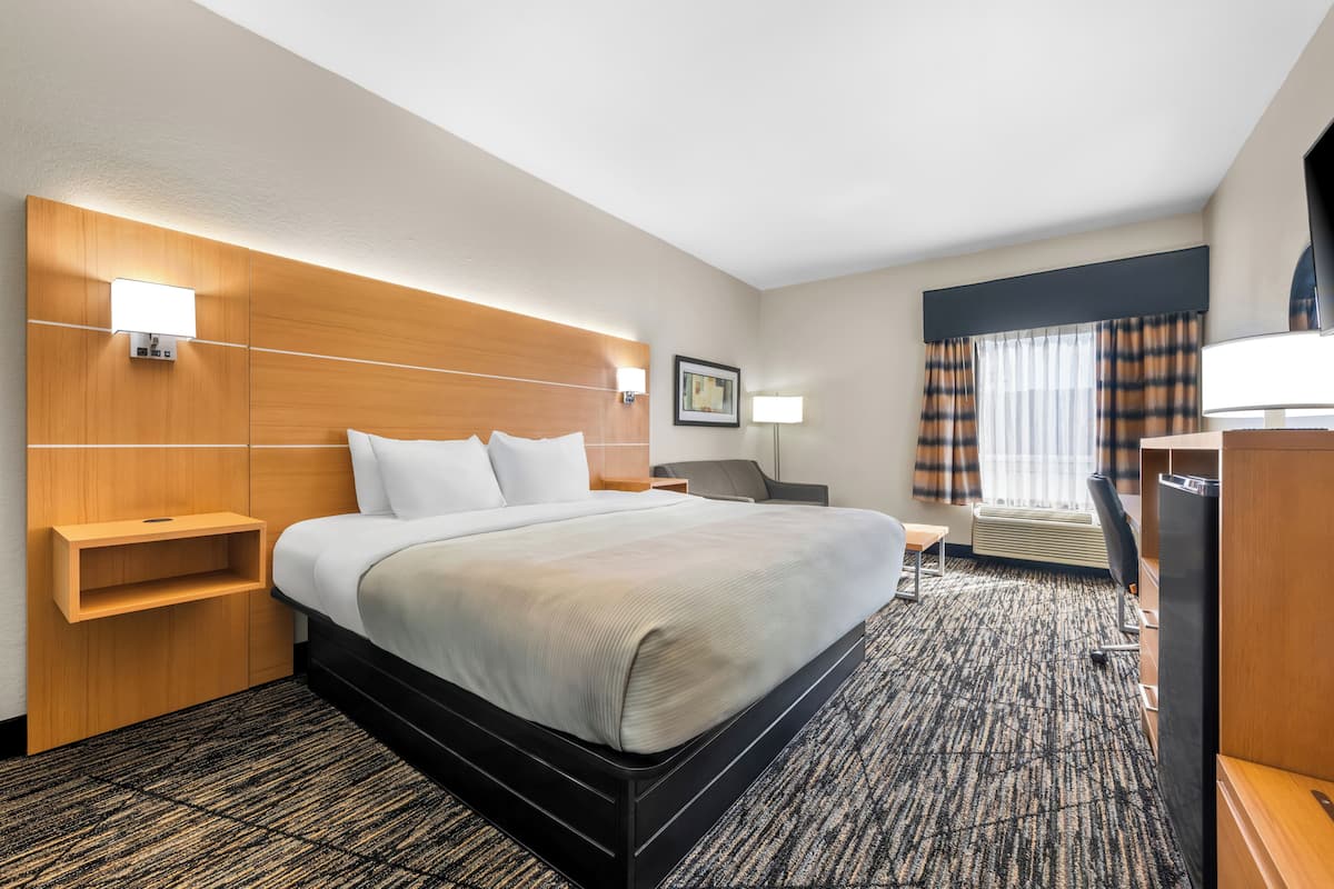 A hotel room with a large bed, bedside tables, a desk, a chair, a TV, and a window with curtains.