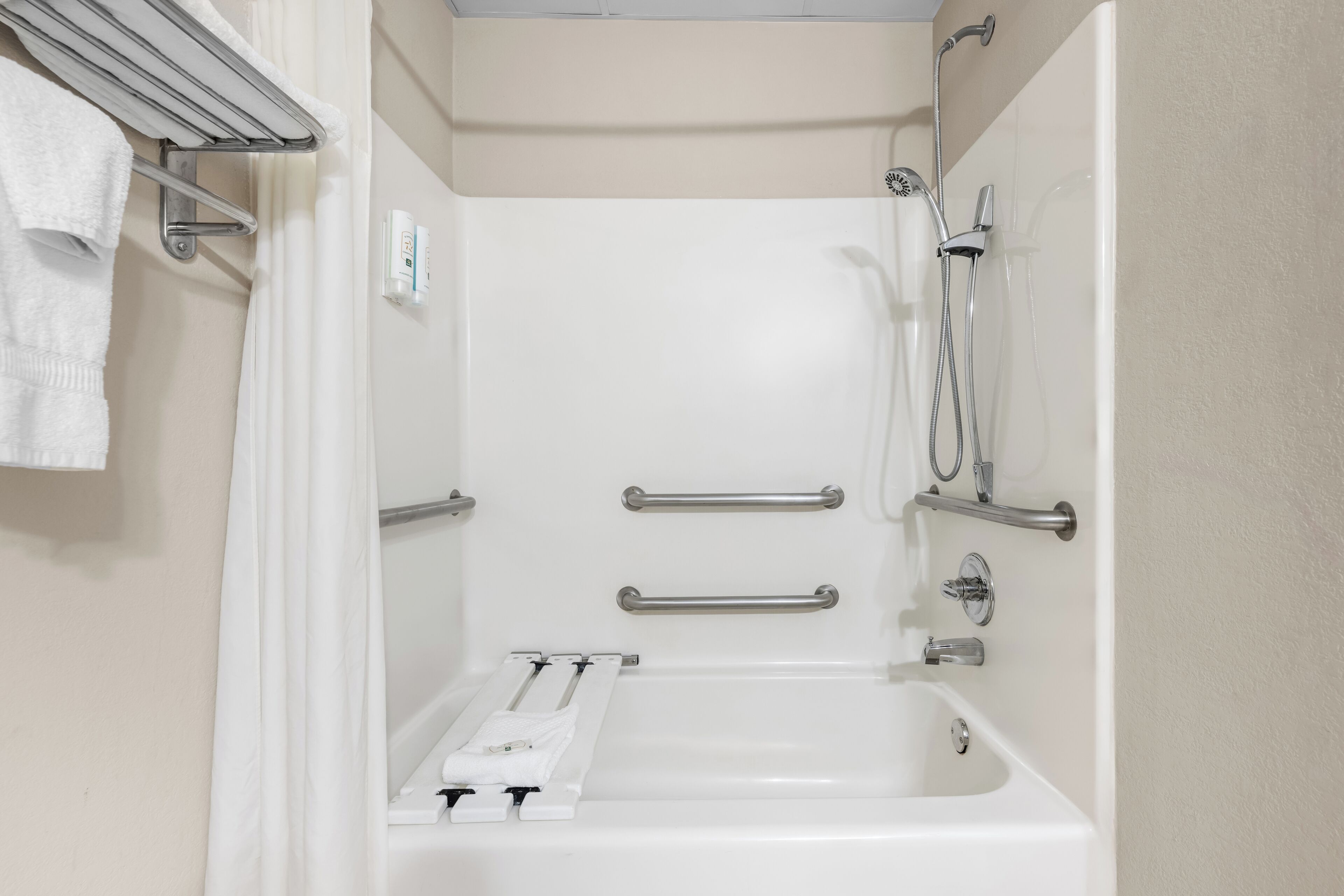 A bathroom with a bathtub, shower, and handrails.