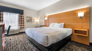 Una habitación de hotel con una cama grande, un escritorio, una silla, una lámpara y un estante en la pared.