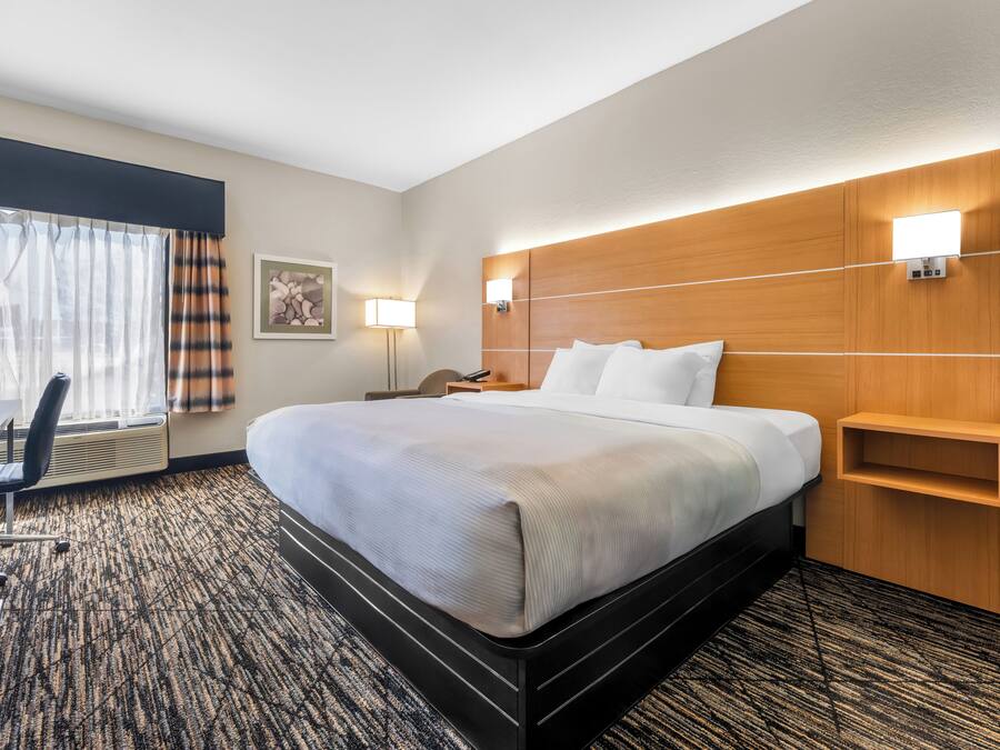 Una habitación de hotel con una cama grande, un escritorio, una silla, una lámpara y un estante en la pared.