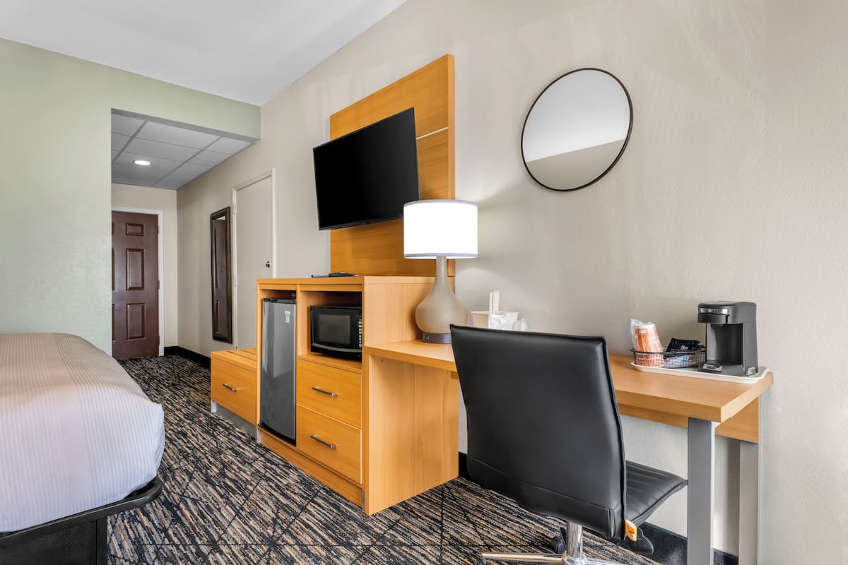 A hotel room with a bed, a desk with a computer, a television, a coffee maker, and a microwave.