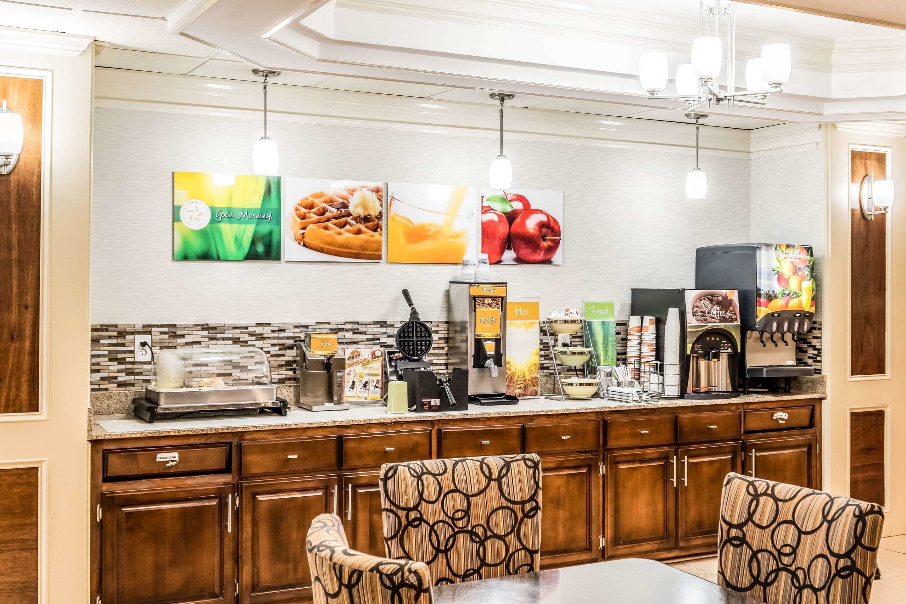 Un bar pour le petit-déjeuner équipé d’un appareil à gaufres, d’une machine à café et de divers aliments. On y trouve des meubles en bois et des chaises à motifs.