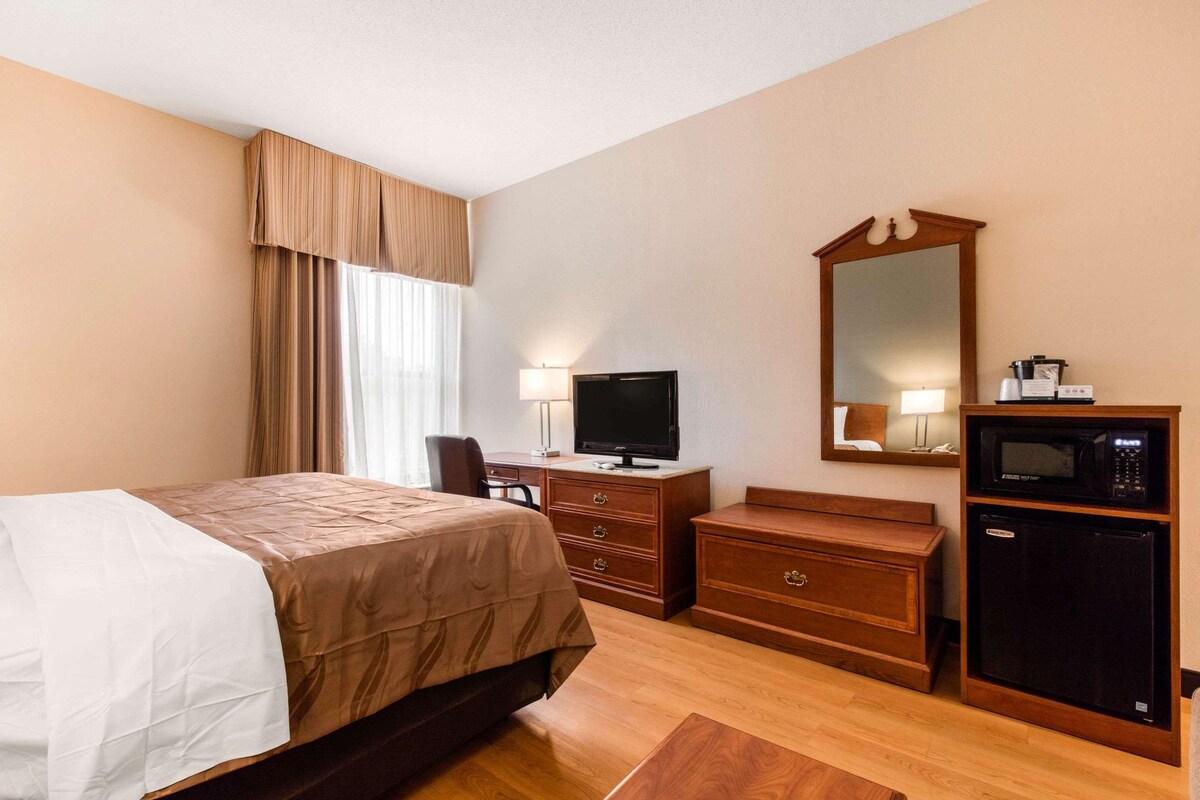 A hotel room with a bed, a desk with a television, a dresser, a mirror, and a microwave.